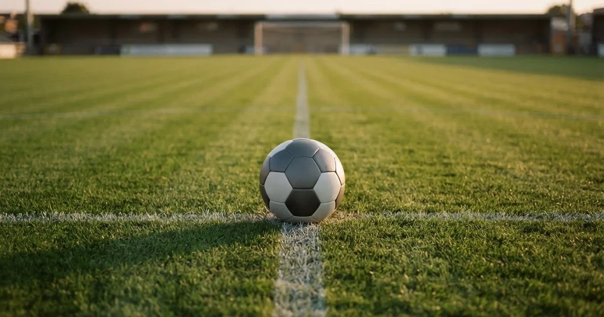Ein Fussball liegt auf dem Mittelkreis eines Rasenfelds, die weissen Linien kreuzen sich auf dem gepflegten Gras im warmen Abendlicht.