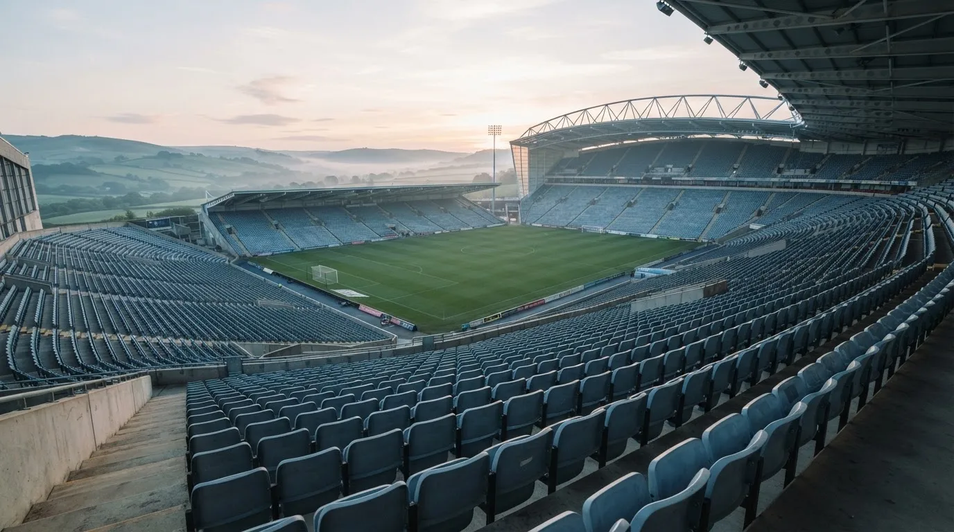 Ein leeres Stadion im Morgenlicht mit Blick auf die Sitzreihen, im Hintergrund Hügel und aufsteigender Nebel.