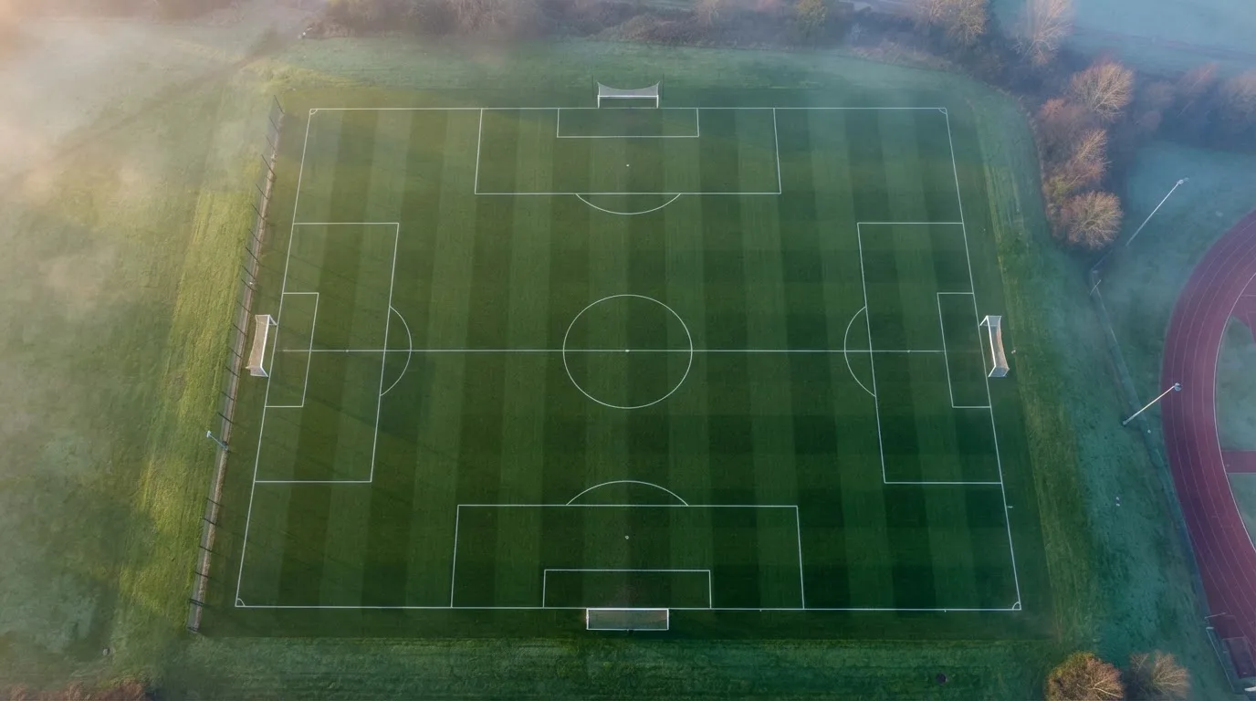 Ein Fussballplatz von oben gesehen, die Linien bilden ein helles Muster auf dem Rasen, Drohnenperspektive in der Morgendämmerung.