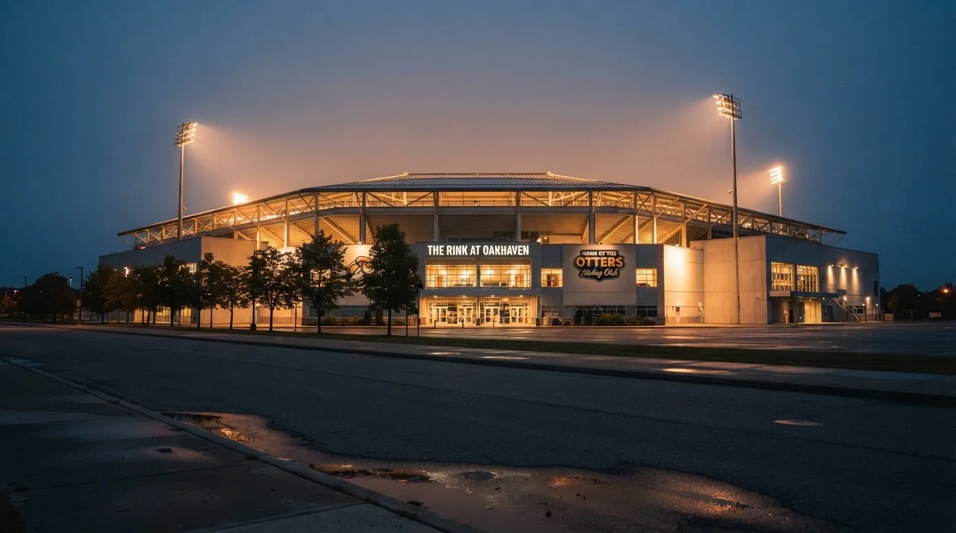 Ein grosses Eisstadion aus der Ferne gesehen, hell erleuchtet von Flutlicht in der Abenddämmerung, davor eine leere Strasse.