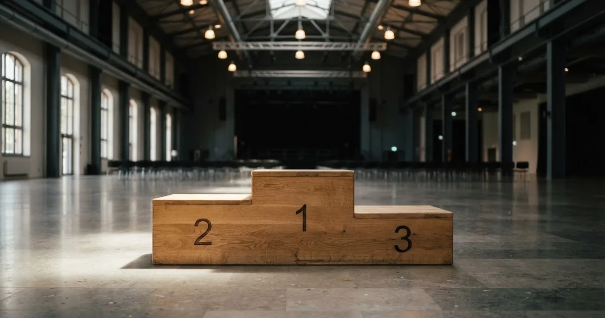 Ein dreistufiges Siegerpodest aus Holz steht in einer leeren Halle, helle Deckenlampen werfen weiche Schatten.