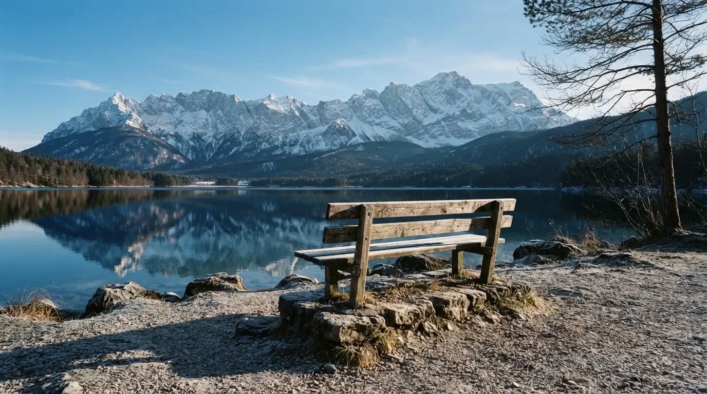 Eine Bank an einem Bergsee, dahinter schneebedeckte Gipfel im klaren Licht eines Wintermorgens.
