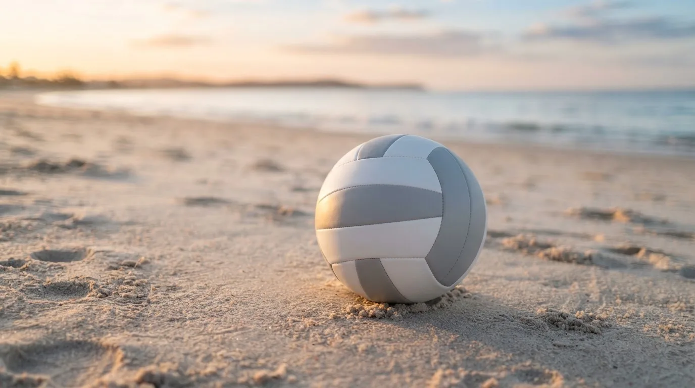 Ein Volleyball liegt auf feinem Sand an einem leeren Strand bei Sonnenaufgang.