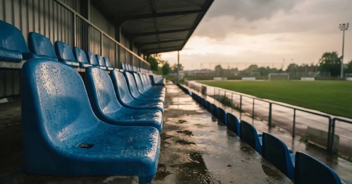 Eine Reihe leerer Sitzschalen auf der Tribüne eines kleinen Stadions, auf den Stufen glänzt Regenwasser.