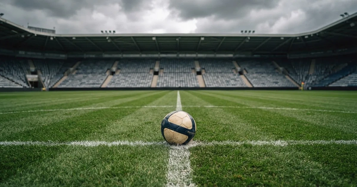 Ein Fussball liegt auf dem Anstosspunkt eines frisch gemähten Rasens, dahinter eine grosse Tribüne unter bewölktem Himmel