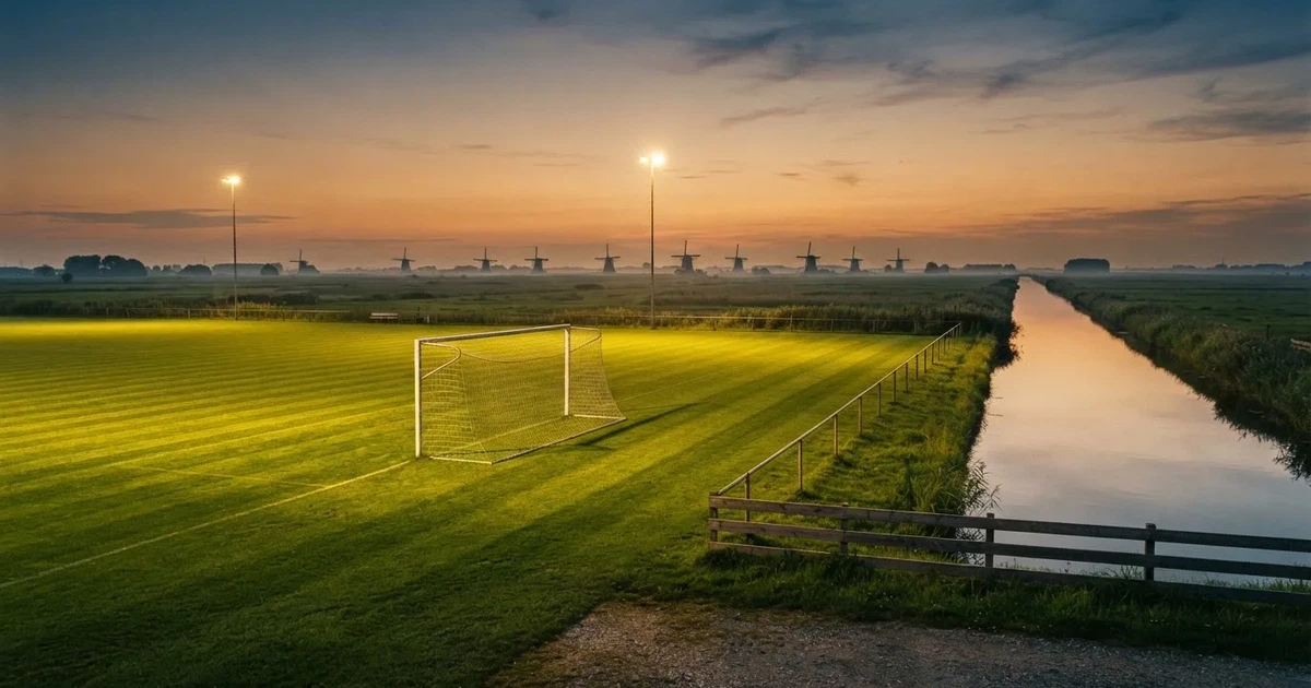 Ein Fussballplatz neben einem Kanal in flachem Land mit Windrädern am Horizont, Abendlicht liegt über dem Rasen