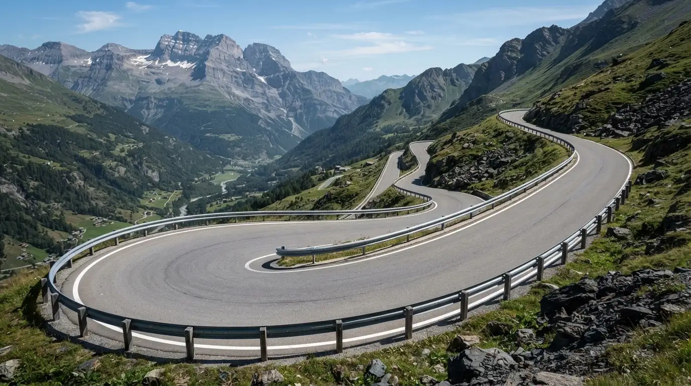 Eine Passstrasse mit Leitplanke windet sich an einem klaren Tag durch eine Berglandschaft.