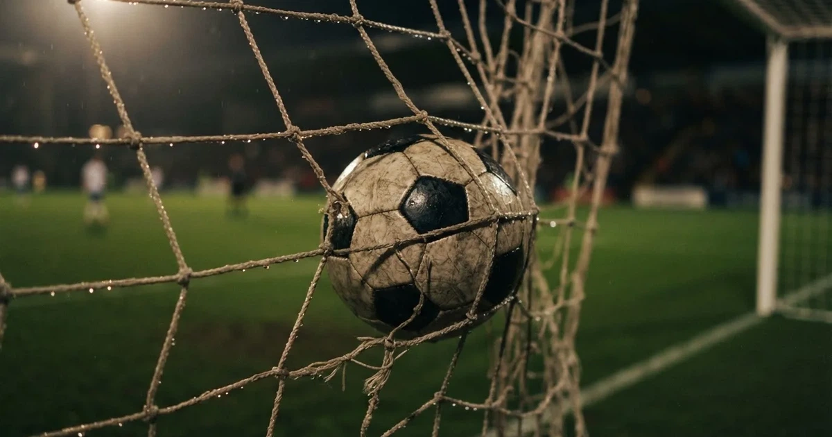 Ein Fussballnetz in Nahaufnahme, in dem ein Ball hängt, Wassertropfen glänzen auf den Maschen.