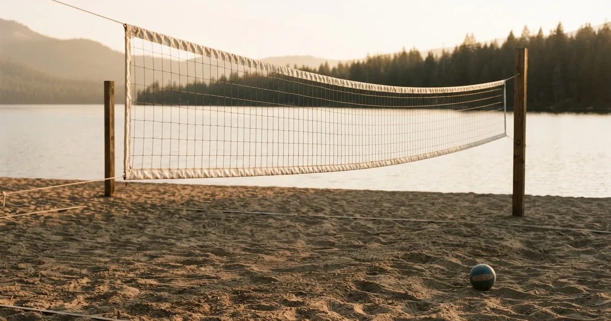 Ein Volleyballnetz am Sandstrand eines Sees, späte Nachmittagssonne, das Wasser liegt glatt im Hintergrund