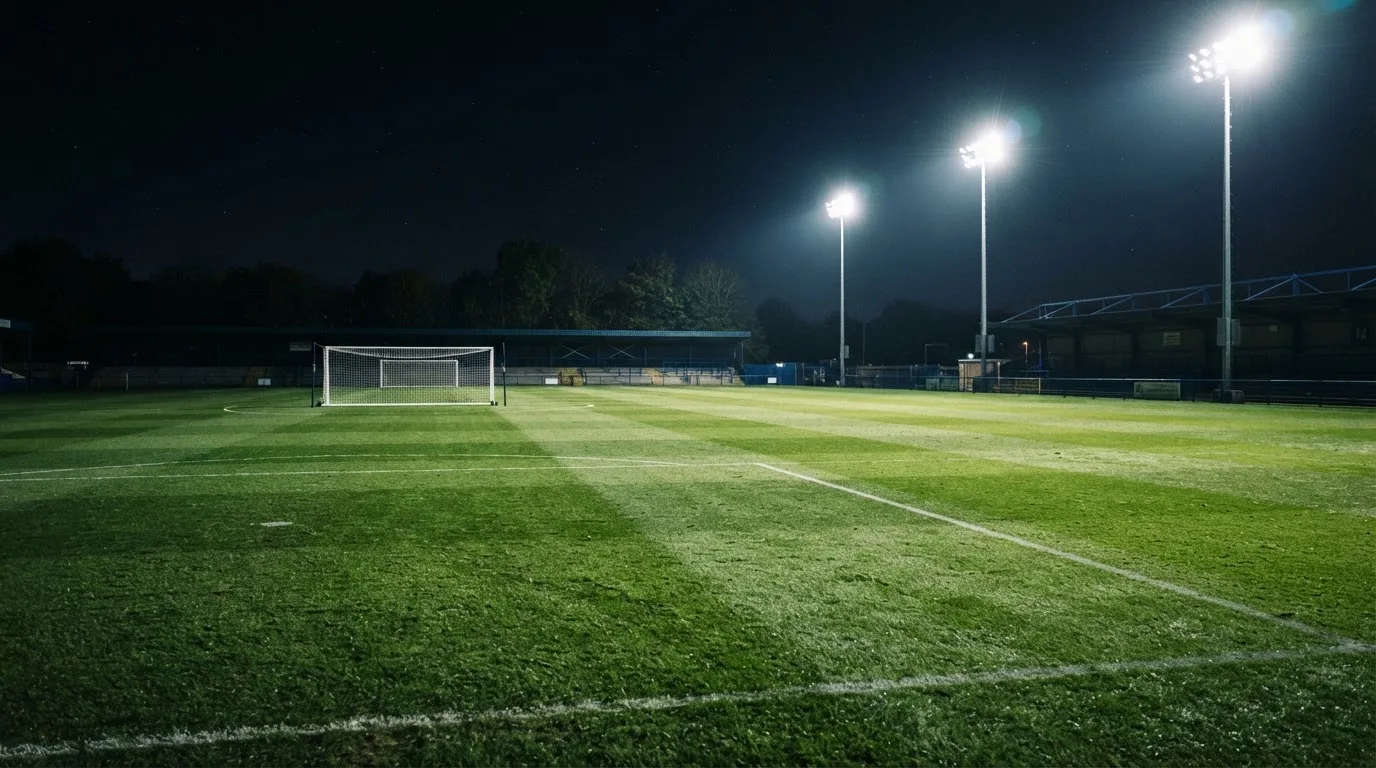 Hohe Flutlichtmasten ragen nachts über einen leeren Trainingsplatz, der Rasen glänzt im weissen Licht.