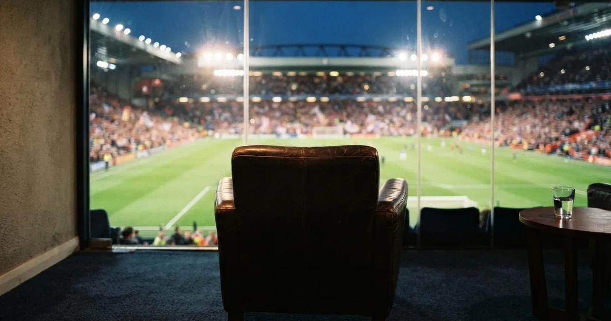 Ein leerer Ledersessel steht in einer Stadionloge mit Blick auf das Spielfeld im Abendlicht.