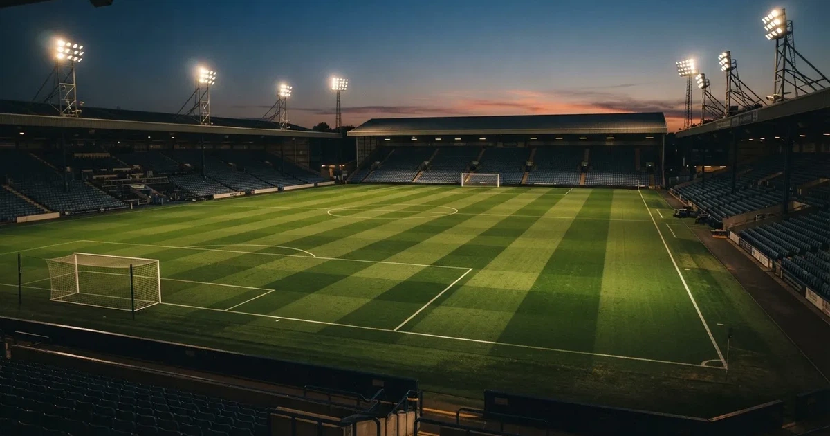 Ein menschenleerer Fussballplatz mit frisch gemähtem Rasen unter Flutlichtmasten in der Abenddämmerung, aus erhöhter Perspektive fotografiert.