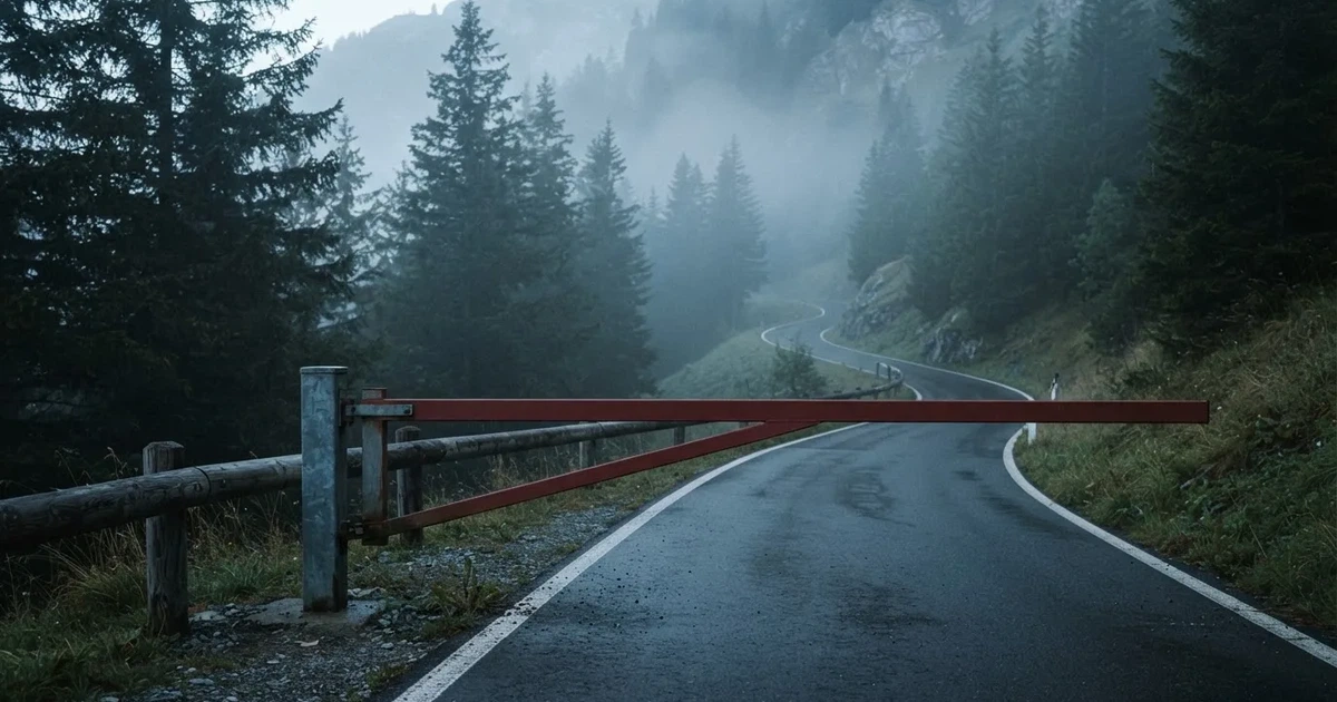 Ein geschlossener Schlagbaum an einer Landstrasse im Gebirge, Morgennebel steht zwischen den Tannen.