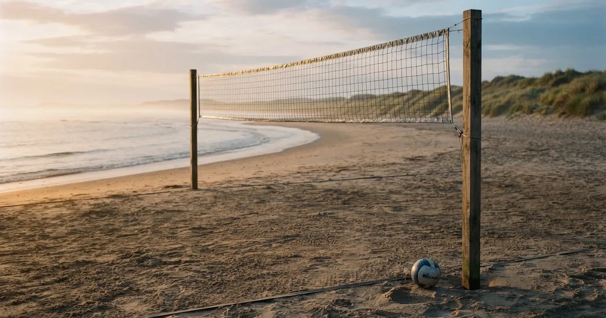 Ein Volleyballnetz spannt sich an einem leeren Sandstrand, das Meer liegt im Dunst.